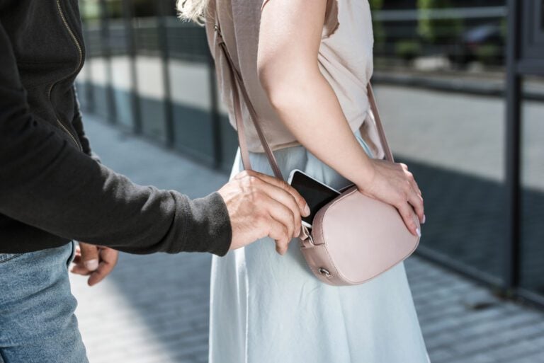 Cropped view of criminal man pickpocketing smartphone from woman's purse